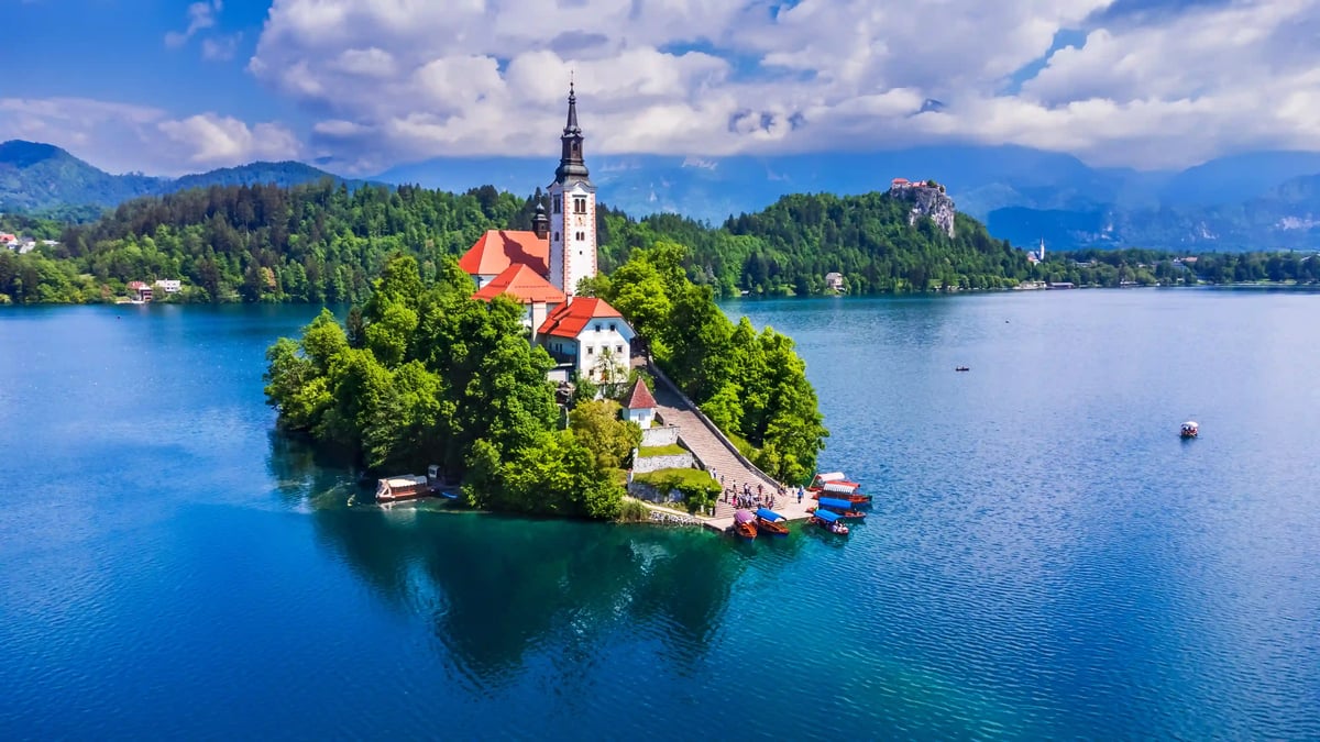Luftaufnahme der Bleder Insel mit Kirche inmitten eines blauen Sees und bewaldeter Hügel