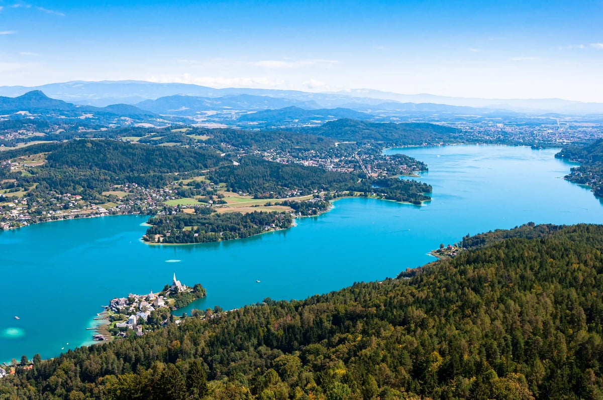 Panoramablick auf den Wörthersee mit türkisfarbenem Wasser, Waldlandschaft und Ortschaften