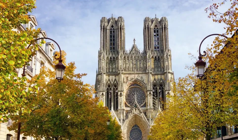 Westfassade der Kathedrale von Reims, eingerahmt von herbstlich gefärbten Bäumen.