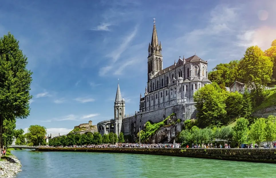 Basilika Unserer Lieben Frau von Lourdes am Fluss Gave vor bewaldeten Hügeln.