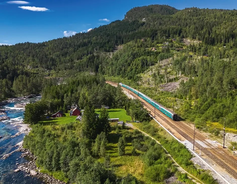 Bergenbahn fährt durch grüne Täler entlang eines Flusses in Norwegen.