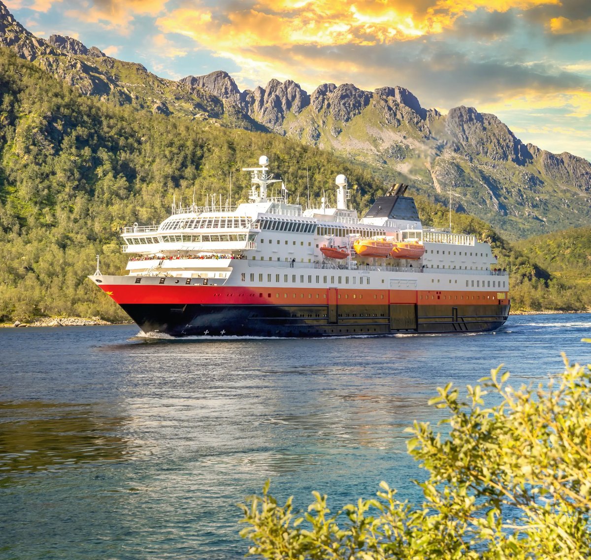 Hurtigruten-Schiff fährt entlang der norwegischen Küste vor beeindruckender Berglandschaft.