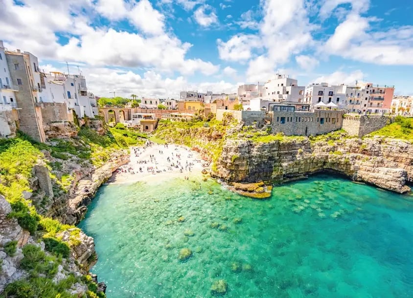 Bucht von Polignano a Mare mit türkisblauem Wasser, Felsen und historischer Altstadt.