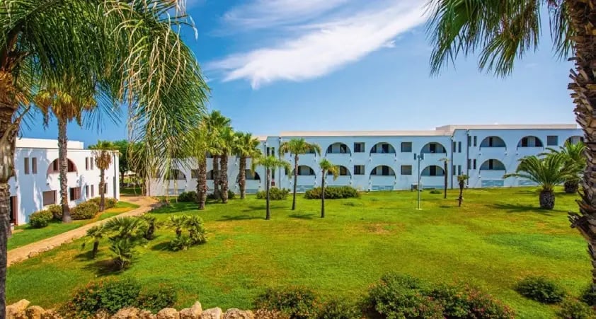 Gartenanlage des Hotels Pietrablu mit Palmen und modernen Gebäuden in Apulien.