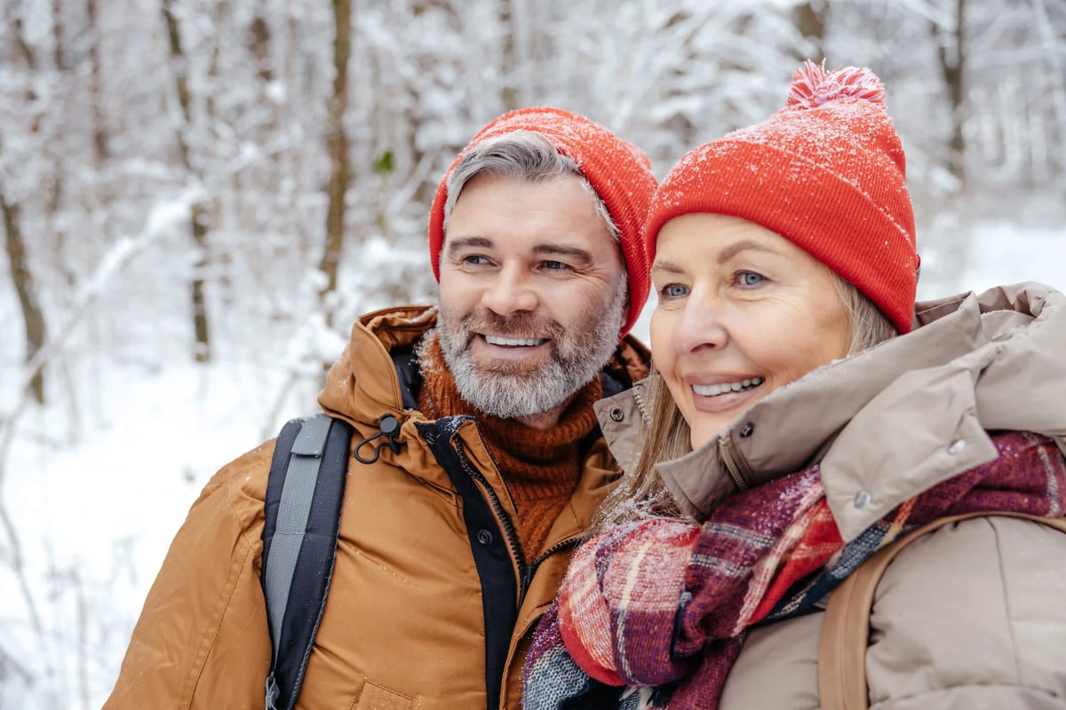 Glückliches Paar bei einem Winterspaziergang durch die verschneite Landschaft Skandinaviens – eingehüllt in warme Winterkleidung inmitten der winterlichen Natur.
