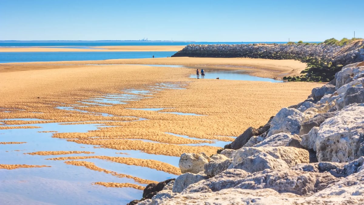 Weitläufiger Sandstrand an der Atlantikküste mit Dünen, Felsen und flachen Wasserläufen.