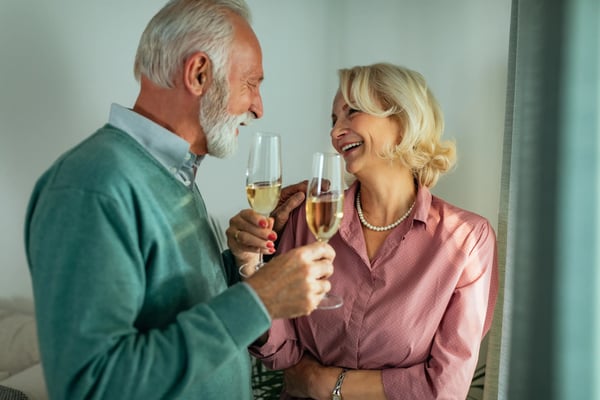 Glückliches älteres Paar stößt mit Weißwein an und genießt gemeinsame Zeit.