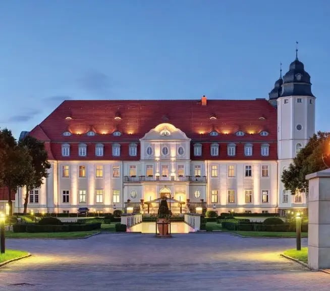 Schlosshotel Fleesensee mit beleuchteter Fassade und gepflegter Gartenanlage in der Abenddämmerung.