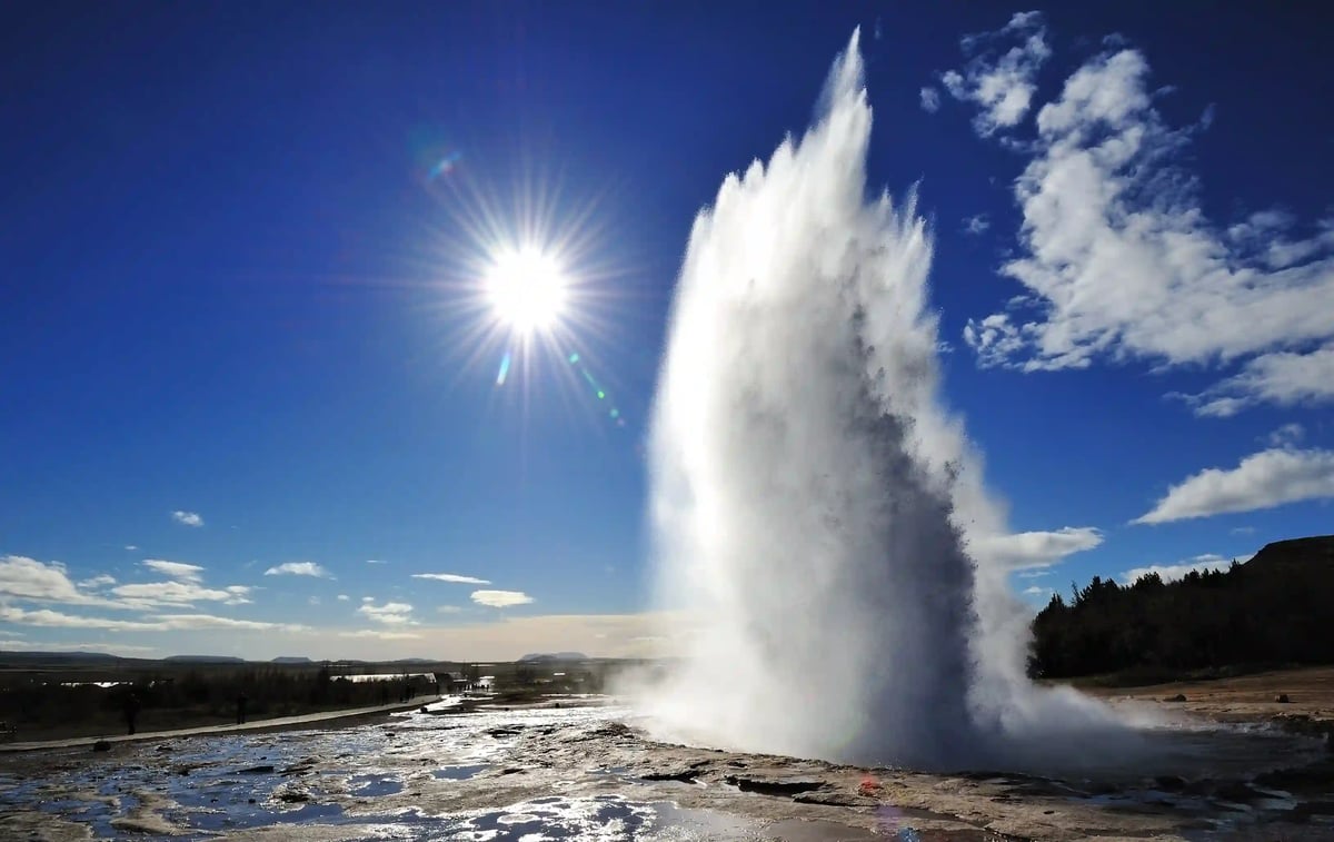 Eindrucksvoller Geysir der eine hohe Wasserfontäne in den Himmel schiesst bei sonnigem Wetter.