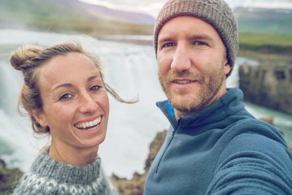 Glückliches Paar macht ein Selfie vor einem grossen Wasserfall in Island.