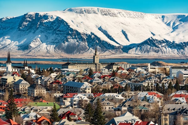 Reykjavik mit bunten Häusern vor schneebedeckten Bergen und Meer im Hintergrund.