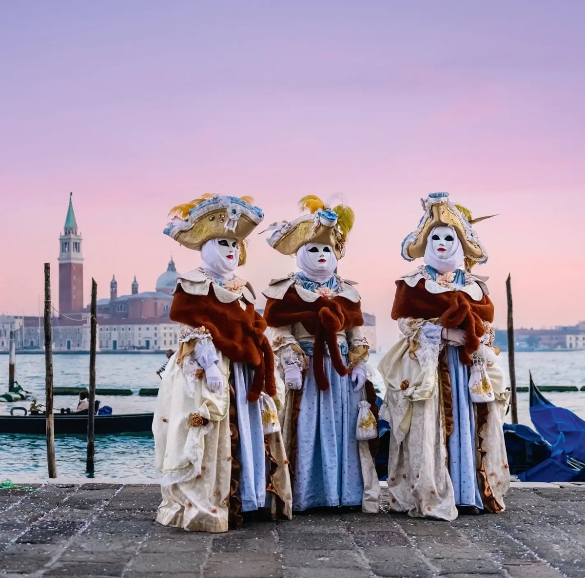 Trois personnes en costumes historiques et masques vénitiens lors du carnaval de Venise, au bord de la lagune.
