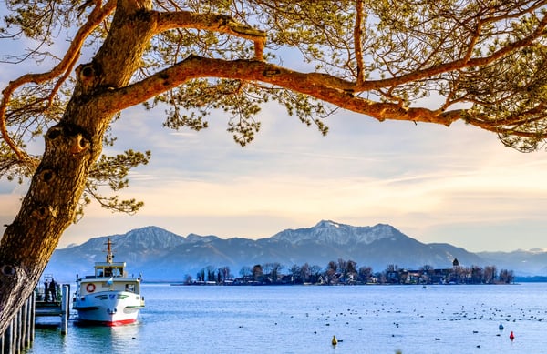 Boot am Chiemsee mit Blick auf die Alpen und ruhiges Wasser unter einem Baum.