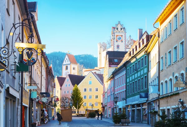 Bunte Häuser in der historischen Altstadt von Füssen mit Blick auf Kirchtürme und Berge im Hintergrund.