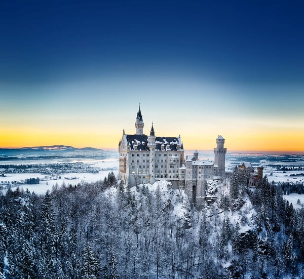 Schloss Neuschwanstein im Winter mit schneebedeckten Bergen und einem See in einer idyllischen Alpenlandschaft.