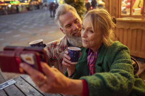 Paar auf einem Weihnachtsmarkt geniesst ein heisses Getränk und macht ein Selfie in festlicher Atmosphäre.