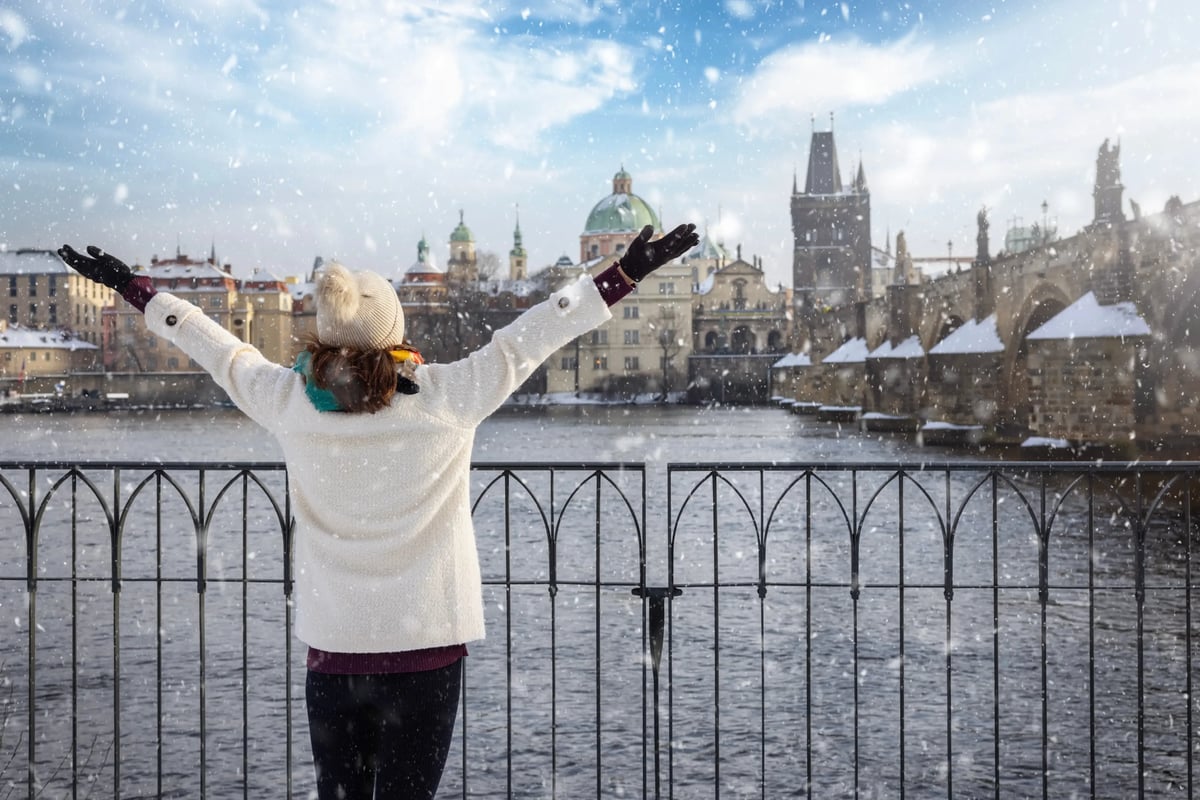 Person mit ausgebreiteten Armen blickt auf verschneites Prag und die Moldau