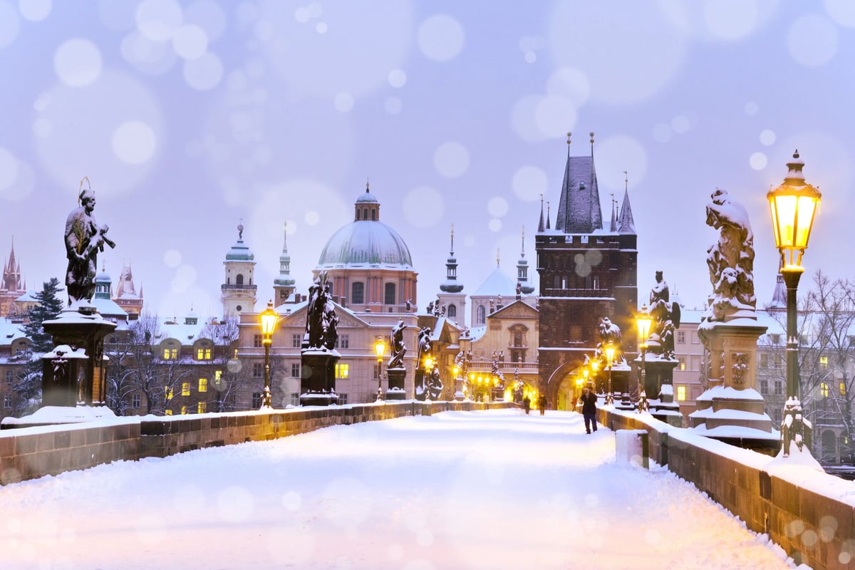 Verschneite Karlsbrücke in Prag mit Laternen und historischen Figuren