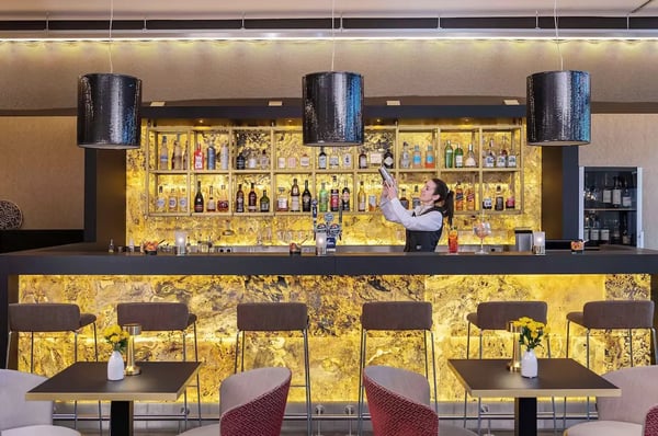 Elegante Hotelbar mit beleuchtetem Tresen und Barkeeperin beim Mixen eines Cocktails.