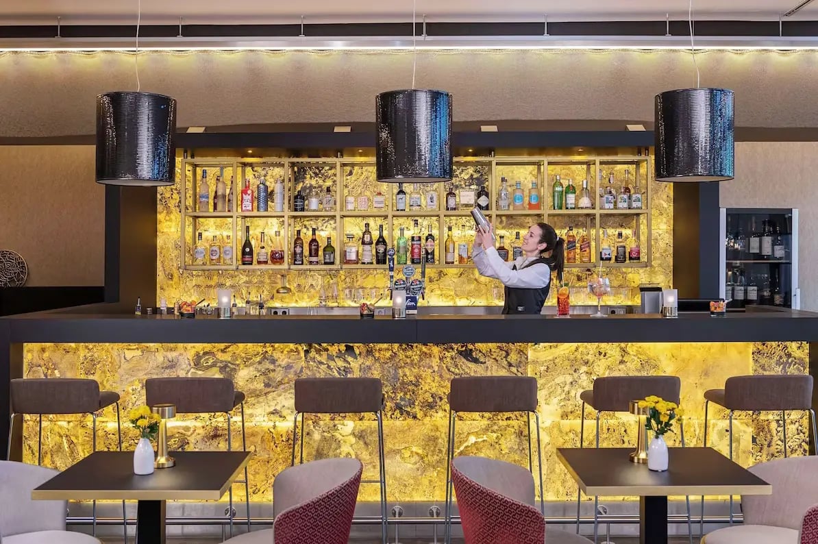 Elegante Hotelbar mit beleuchtetem Tresen und Barkeeperin beim Mixen eines Cocktails.