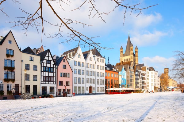 Bunte Häuser der Kölner Altstadt am Rhein mit verschneiter Promenade und Kirche im Hintergrund.