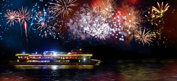Ausflugsschiff auf dem Rhein bei Nacht mit Feuerwerk am Himmel.