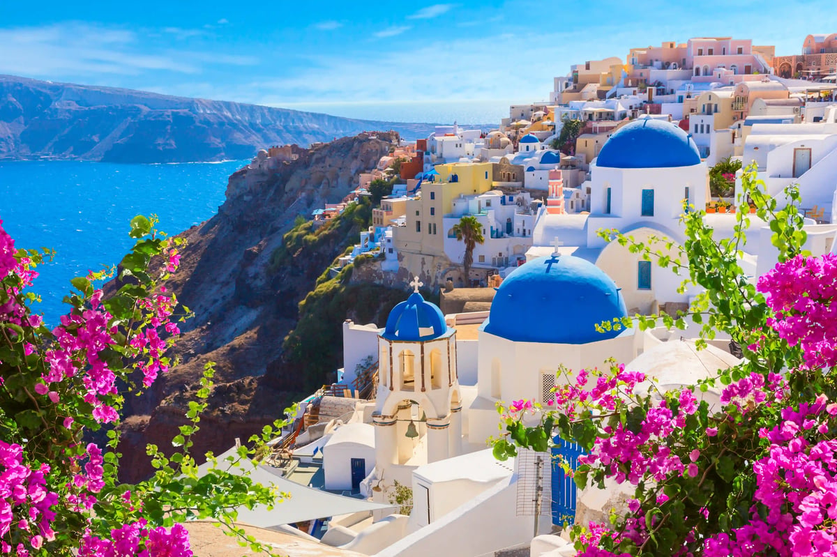 Weisse Häuser und blaue Kuppelkirchen auf Santorini mit Blick auf die Caldera und das Meer