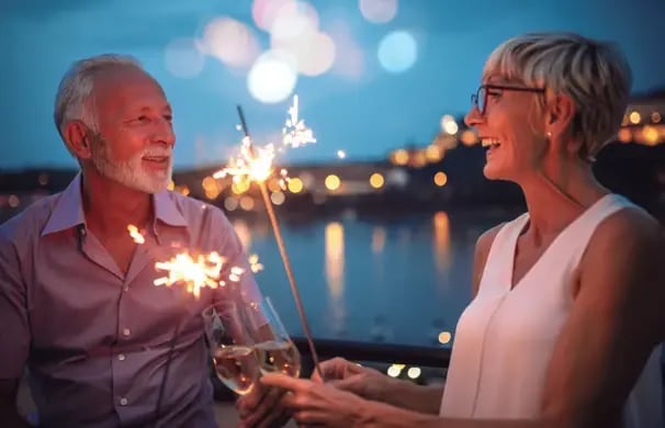 Paar stößt mit Sekt an und hält Wunderkerzen während einer festlichen Abendstimmung an Bord.