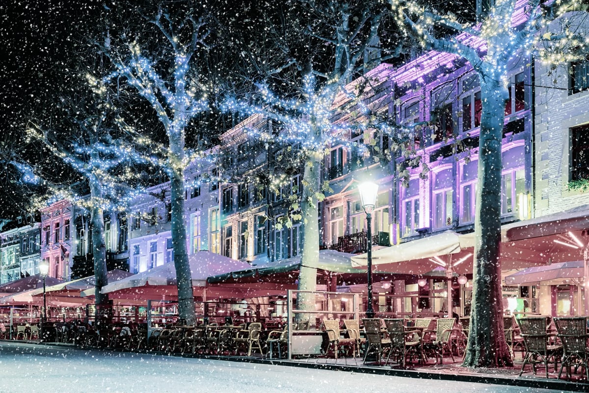 Rue hivernale à Maastricht avec des arbres illuminés, des terrasses couvertes de neige et une ambiance festive.