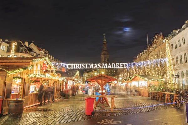 Weihnachtsmarkt bei Nacht mit beleuchteten Holzständen, Lichterketten und Besuchern unter dem Schriftzug Christmas Market.