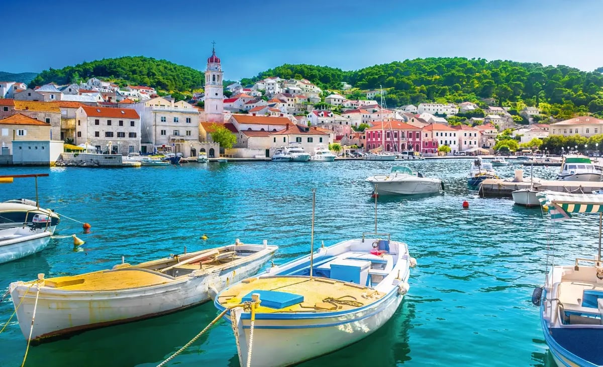 Bateaux de peche dans le port de Pucisca sur l ile de Brac, devant une ville cotiere avec un clocher et des collines verdoyantes en arriere plan.