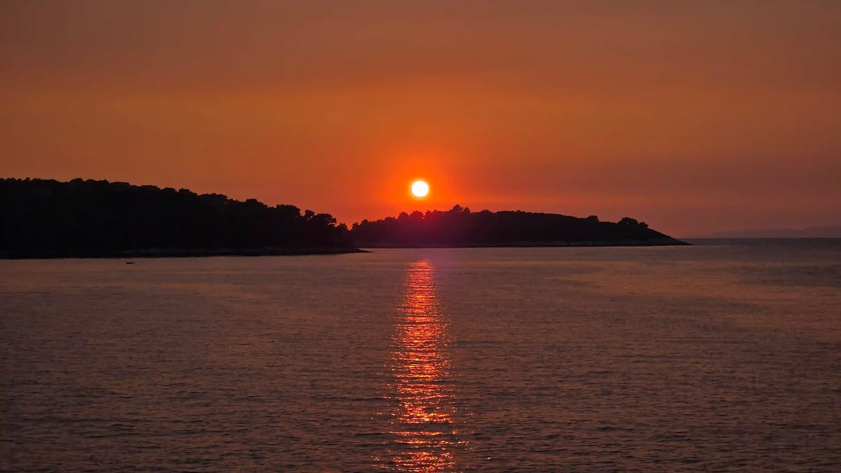 Soleil rouge à l’horizon au-dessus de la mer Adriatique, avec la silhouette d’une île