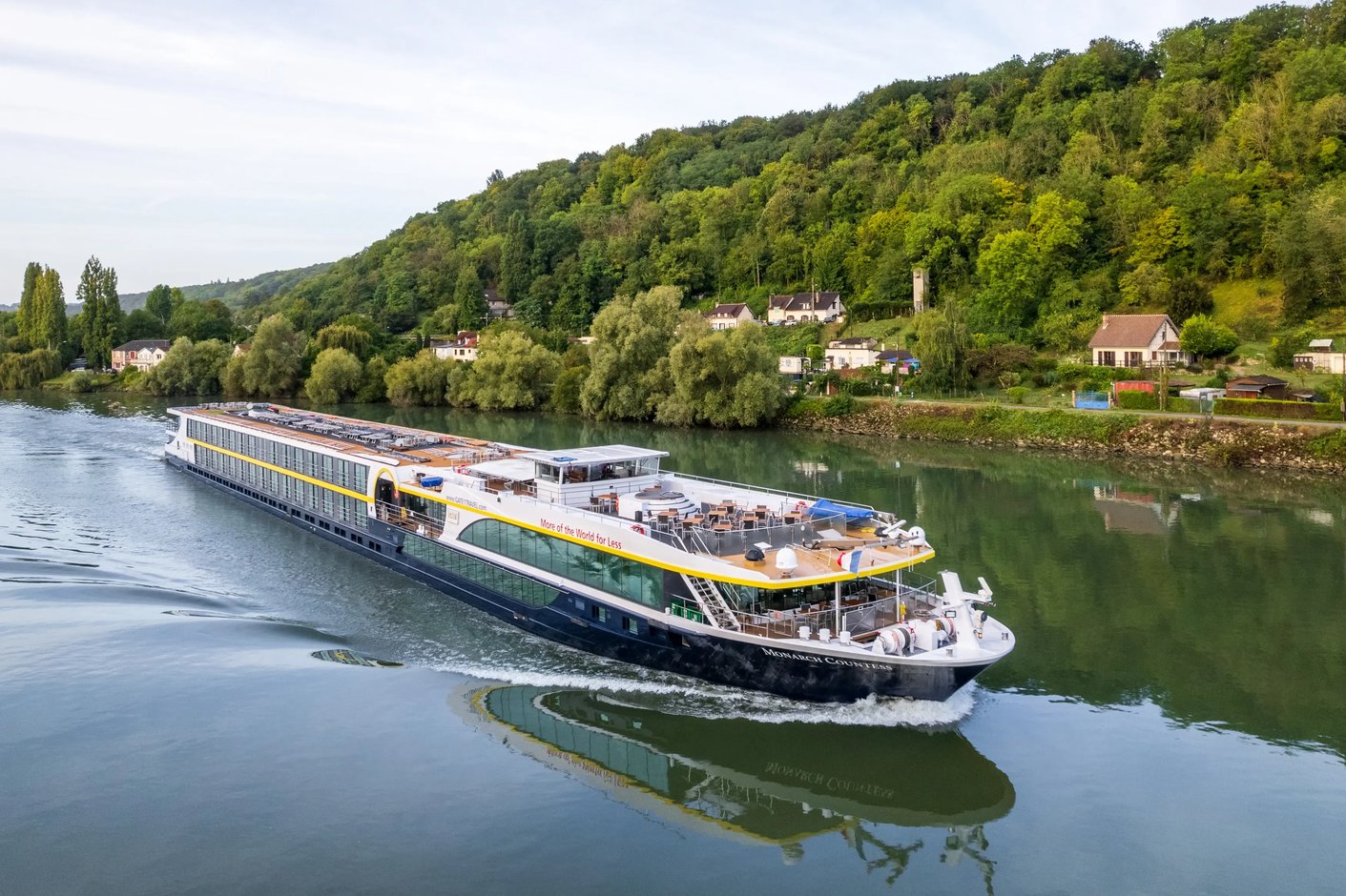 Le MS Monarch Countess navigue sur une riviere calme le long de rives boisees et d un village rural.