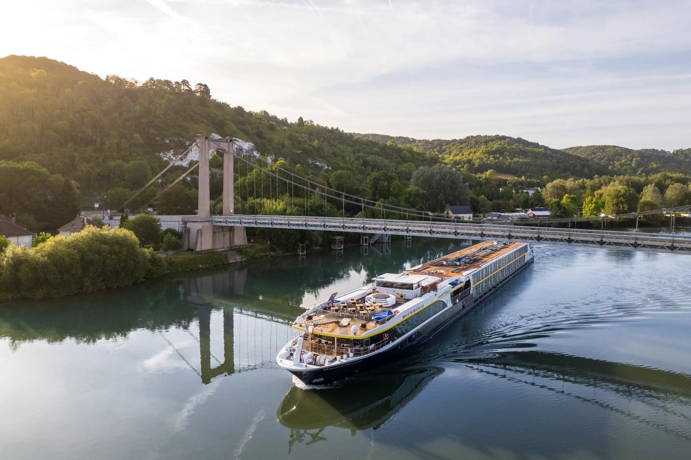Le MS Monarch Countess passe sous un pont suspendu sur une riviere paisible au coeur d un paysage vallonne verdoyant.