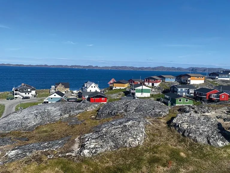 Maisons en bois colorées dans un paysage côtier rocheux au Groenland, sous un ciel bleu éclatant avec vue sur la mer.