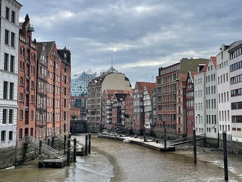 Blick auf einen Fleet in der Hamburger Speicherstadt bei Ebbe, flankiert von historischen Backsteinspeichern, mit der Elbphilharmonie im Hintergrund