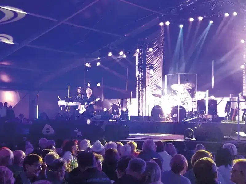 Konzertbühne mit Band, Scheinwerfern und Publikum im Vordergrund