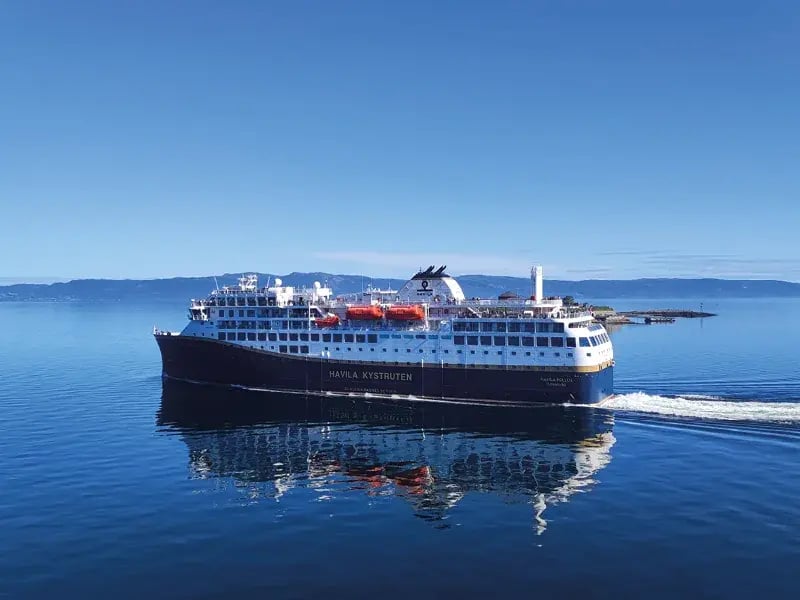 Passagierschiff fährt auf ruhigem Meer, Küstenlinie im Hintergrund unter klarem Himmel