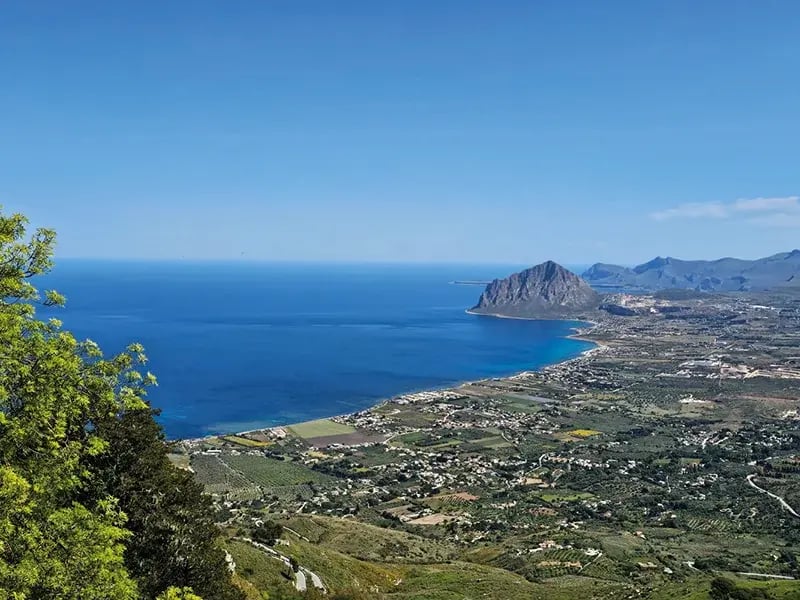 Vaste paysage côtier avec mer, champs et montagnes sous ciel clair