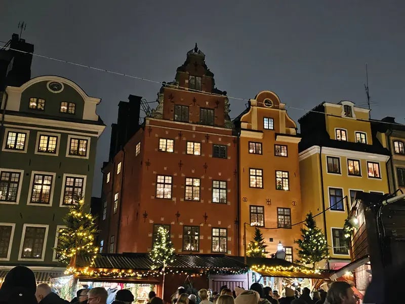 Historische Häuser bei Nacht mit beleuchteten Fenstern und Weihnachtsmarkt im Vordergrund