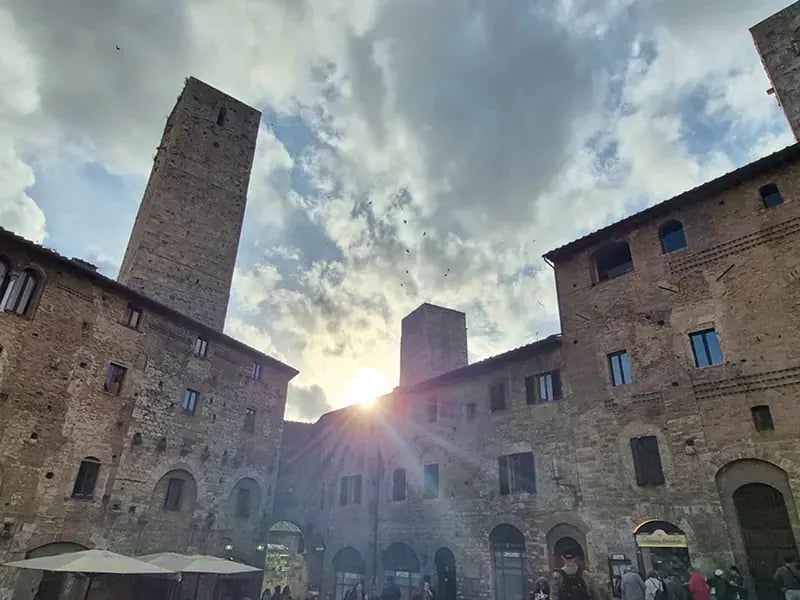 Historischer Platz mit steinernen Gebäuden und hohen Türmen, Sonne scheint zwischen den Gebäuden