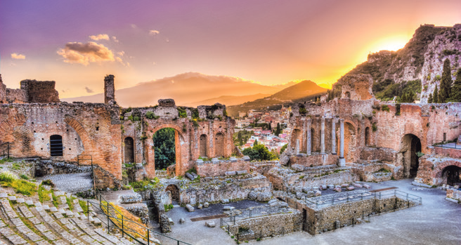 Ruinen des antiken Theaters von Taormina mit Blick auf die Stadt und die Berge im Abendlicht.