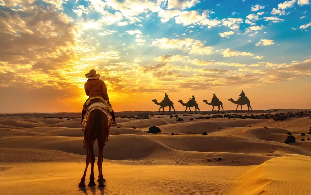 Kamelritt durch die Thar Wüste bei Jaisalmer in Rajasthan mit beeindruckender Dünenlandschaft bei Sonnenuntergang.