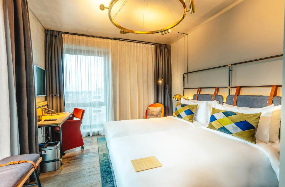 Stilvolles Hotelzimmer mit großem Bett, Sitzbank am Fußende, Nachttischlampen und schlichter, moderner Einrichtung.