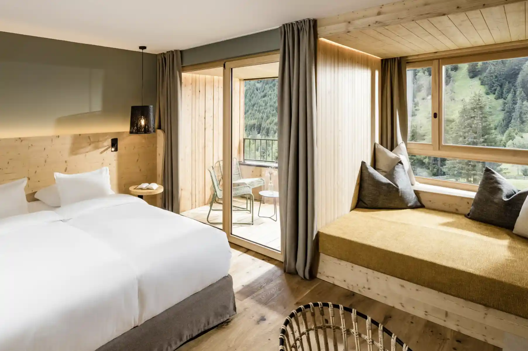 Modernes Hotelzimmer mit Doppelbett, Holzdetails, Sitzbank am Fenster und Balkon mit Blick auf die Berge in Südtirol