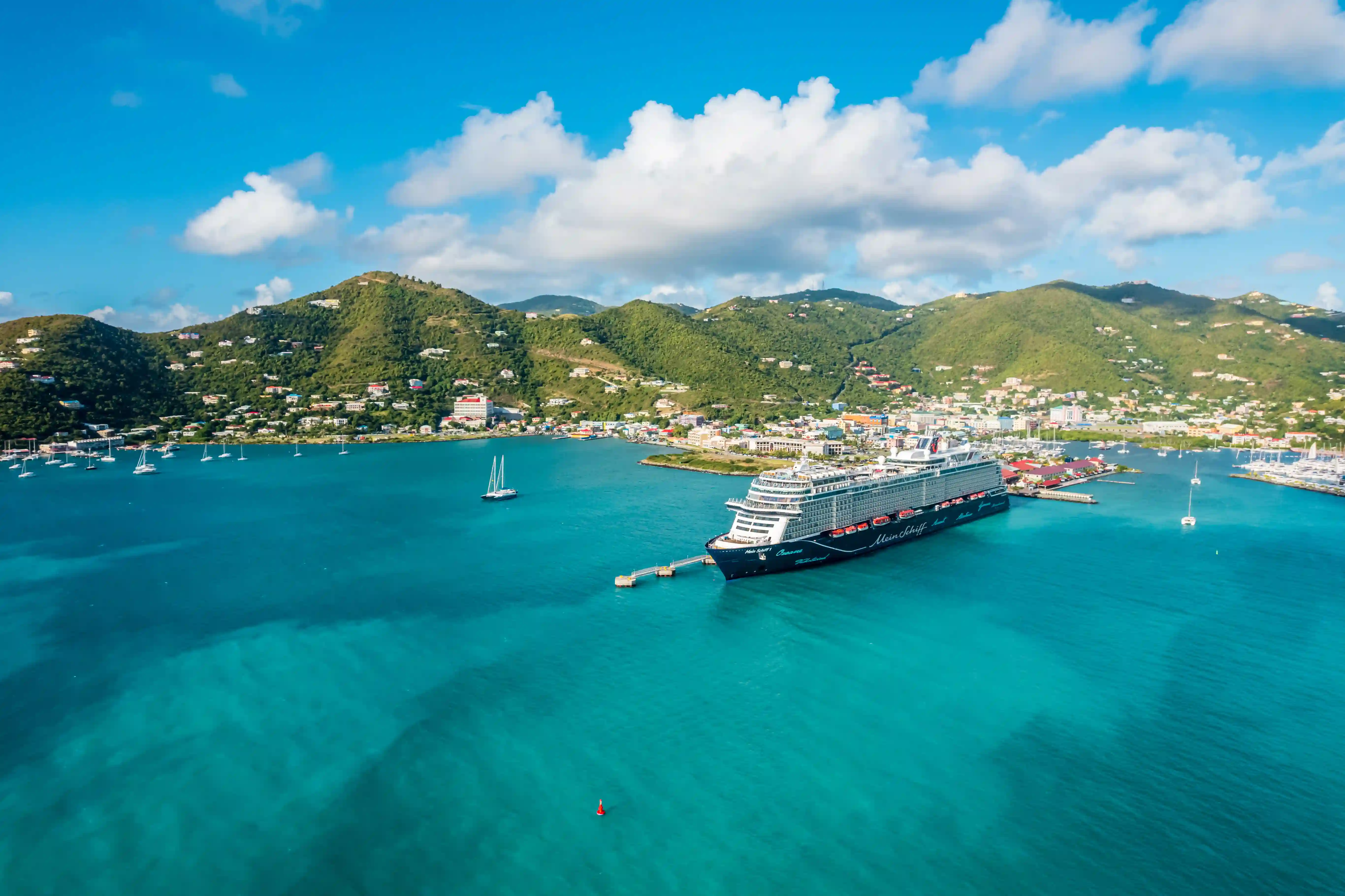 Kreuzfahrtschiff im Hafen mit tuerkisfarbenem Meer, Anlegesteg und gruener Huegellandschaft im Hintergrund