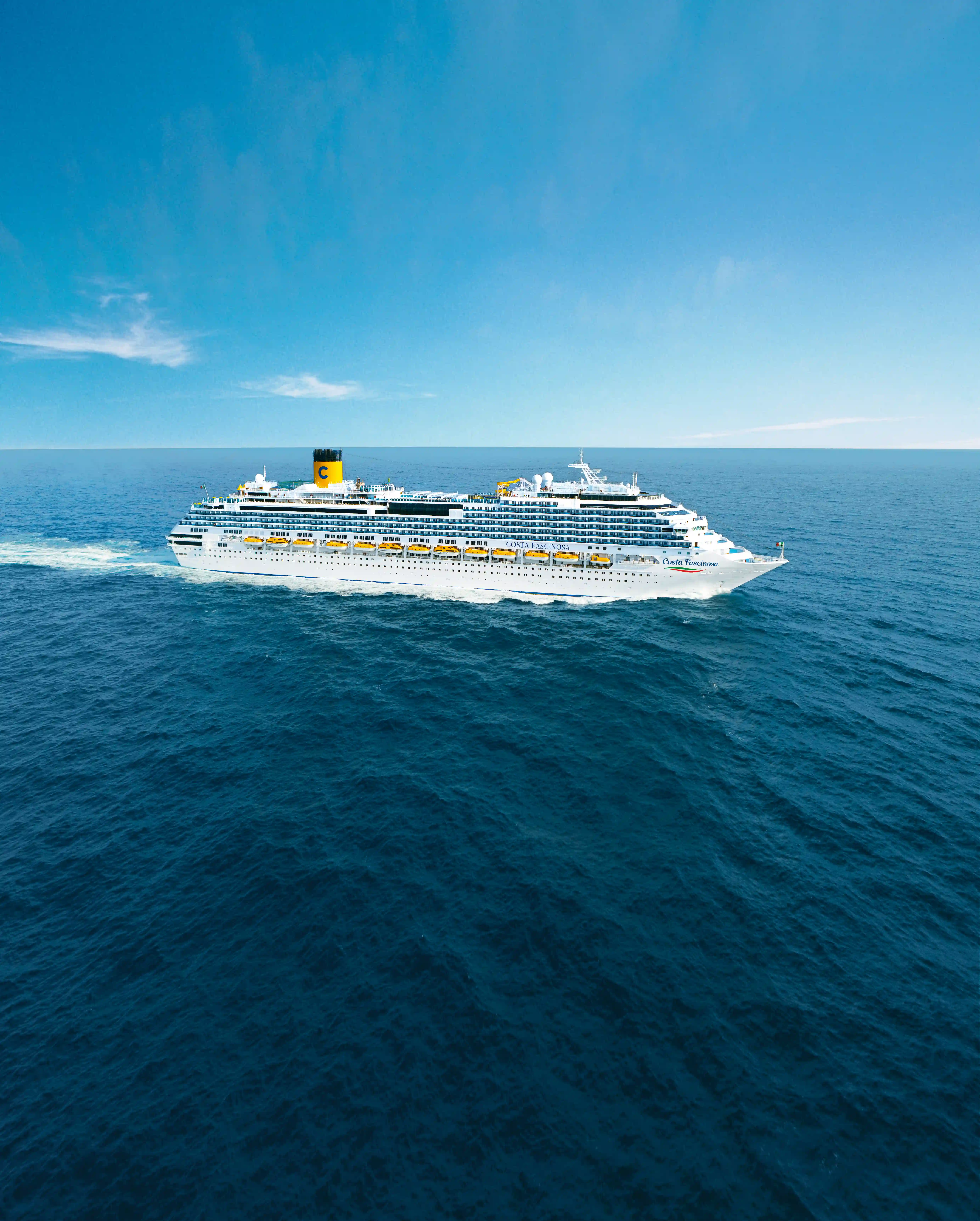 Großes Kreuzfahrtschiff Costa Diadema fährt bei ruhiger See unter blauem Himmel, Seitenansicht mit mehreren Decks und gelben Rettungsbooten