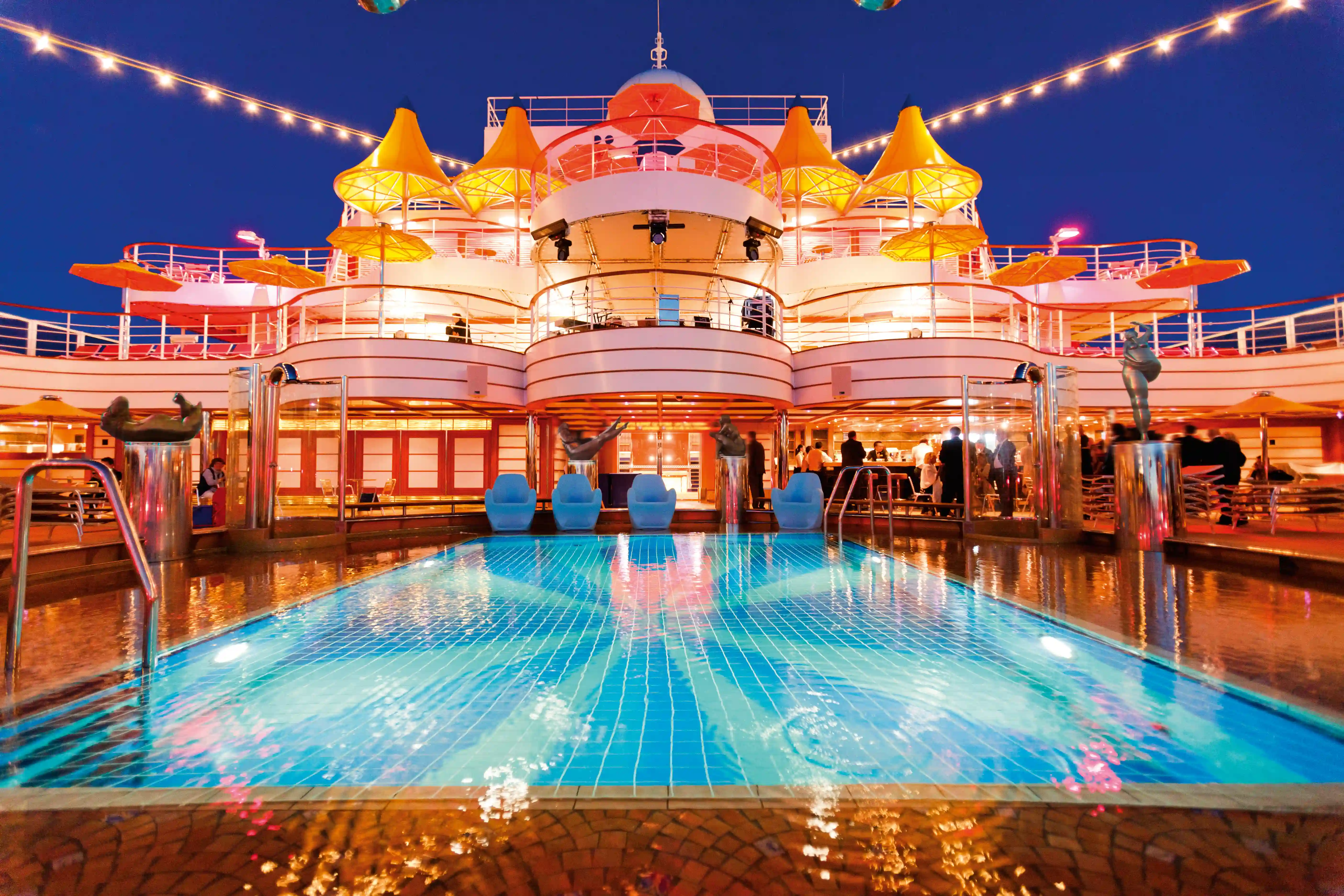 Beleuchteter Poolbereich bei Nacht mit Sitzgelegenheiten und Oberdecks