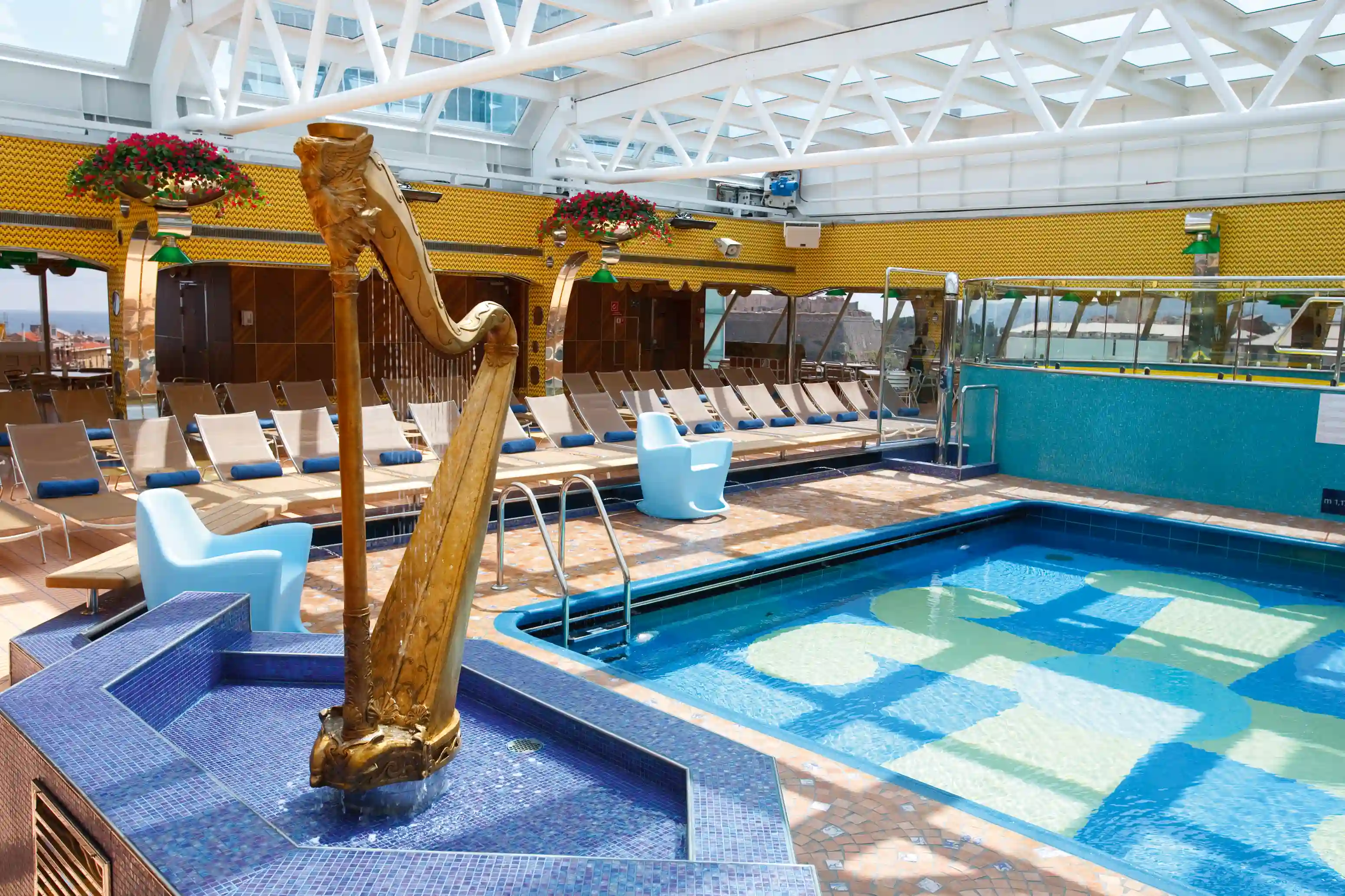 Aussenpooldeck mit einem Schwimmbecken, einer dekorativen goldenen Harfe als Wasserspiel und Reihen von Sonnenliegen