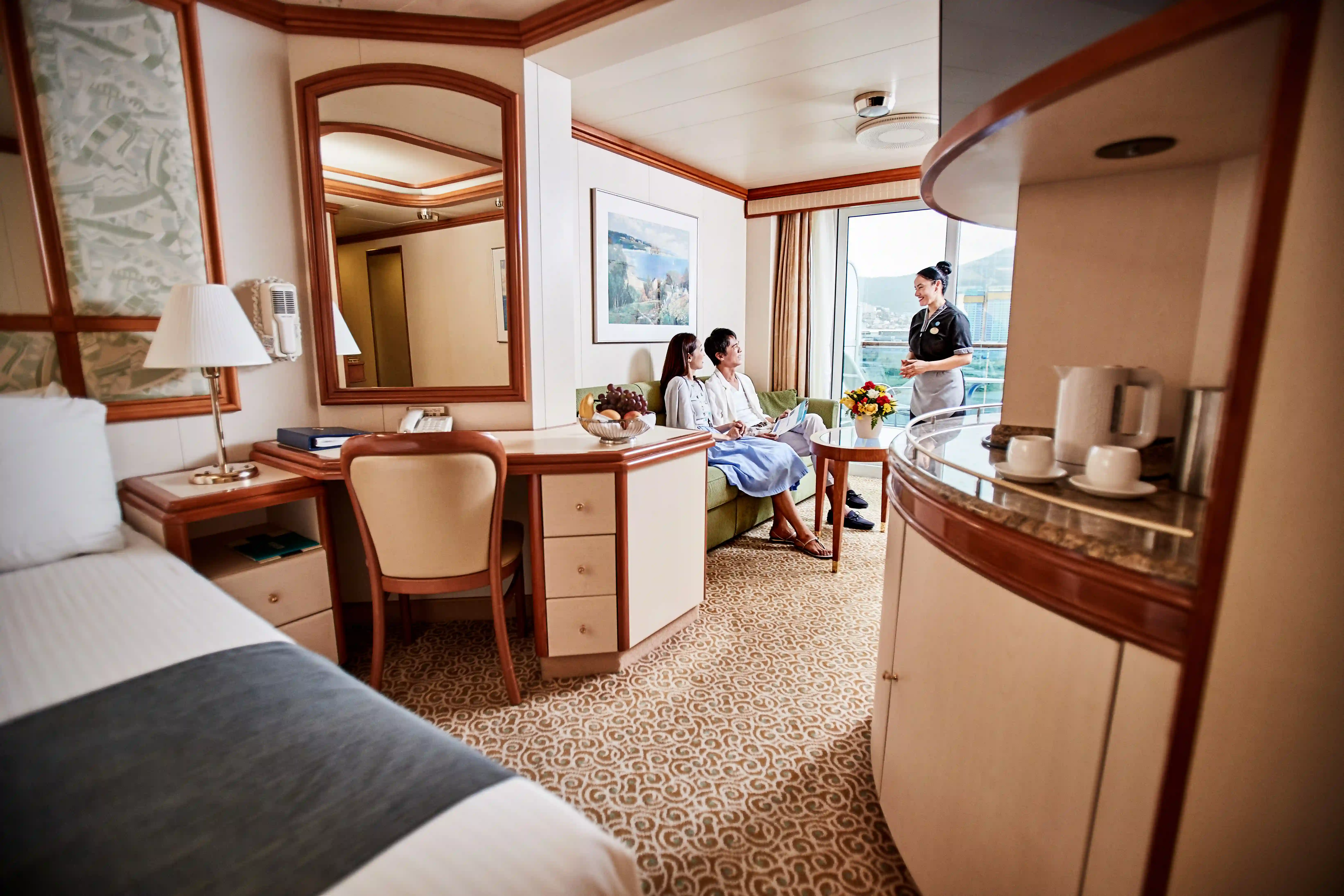 Gäste sitzen in der Mini Suite während eine Crew Mitarbeiterin Service erklärt